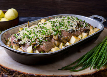 Schnitzel mit Apfelstücken und Champingnons in einer Gratinform mit Käse überbacken und mit Schnittlauch garniert.