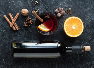 Glühweinflasche auf Steintisch, mit Glas gefüllt mit Glühwein. Rundherum Gewürze und halbe Orange